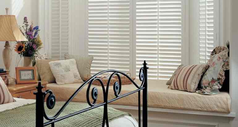 Plantation shutters in a white bedroom bay window.